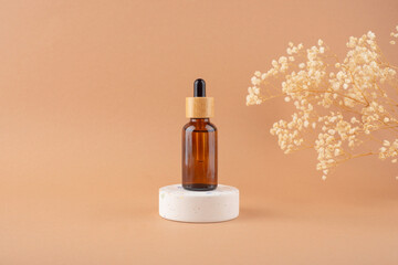 Amber glass dropper bottle with bamboo lid on white podium for product presentation on beige background with dry plants. Skincare products ,natural cosmetic. Beauty concept for face and body care
