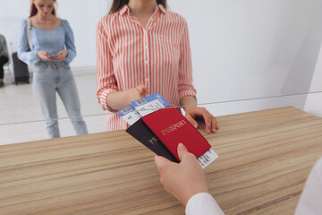 Agent giving passports with tickets to client at check-in desk in airport, closeup