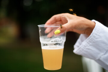 Wasp sits on a woman's hand holding a glass with a drink