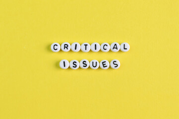 Alphabet beads with text CRITICAL ISSUES isolated on a yellow background