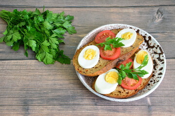 sandwiches made of whole grain bread with boiled eggs, tomato slices and parsley on white and brown plate on dark wooden background