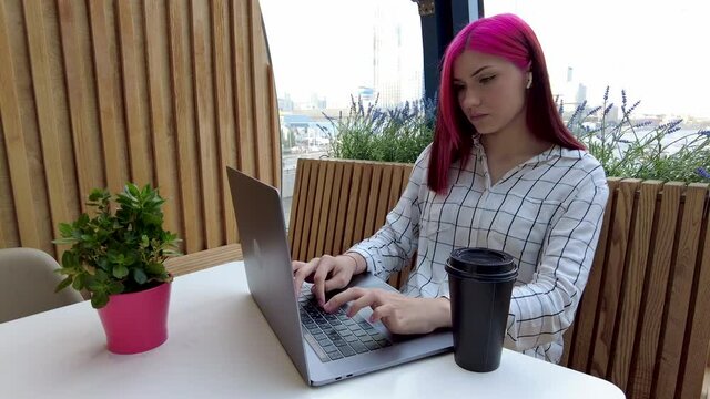 Beautiful red-haired student girl drinking coffee and works as remote employee with laptop in cafe. High quali ty 4k footage