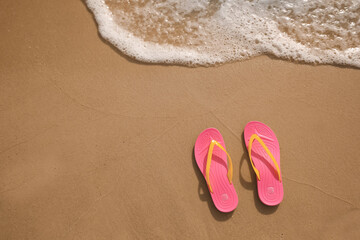 Fototapeta na wymiar Bright pink beach slippers on sand near sea, top view. Space for text
