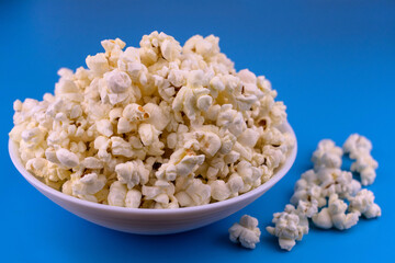 A bowl of popcorn on a blue background. Close-up.