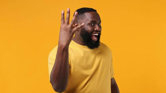 Cheery young african american man 20s wears orange t-shirt countdown 1 2 3 one two three go celebrate win scream rejoices doing winner hands gesture isolated on plain yellow background studio portrait