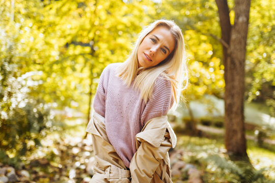 Caucasian blonde woman smiling happily on sunny autumn or spring day outside walking in park.