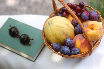 Vintage basket full of various fruit, hardback book and retro sunglasses on picnic basket. Selective focus.
