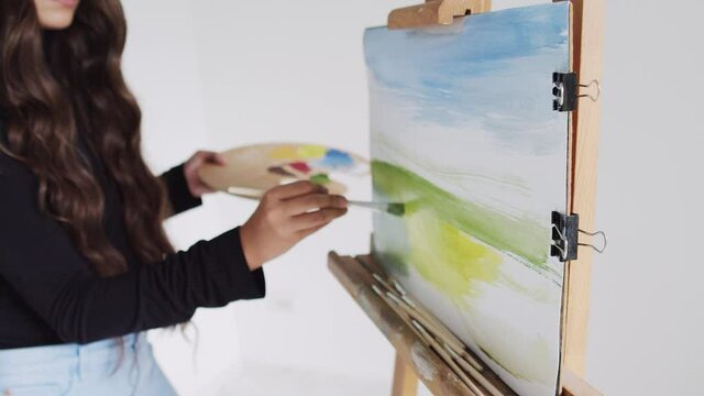 Young woman artist painting picture on canvas in art studio