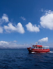 Small red fishing boat in blue sea water. Silhouettes of islands on background.