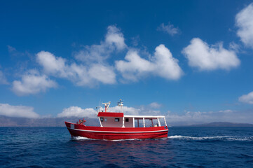 Small red fishing boat in blue sea water. Silhouettes of islands on background.