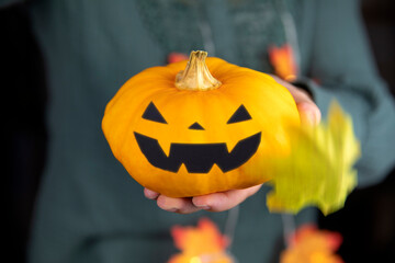 orange pumpkin head for Halloween in hand. scary head Jack o lantern with autumn leaves falling. spooky smile horror