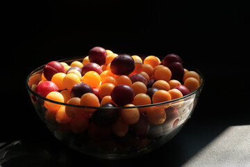 Ripe cherry plum of different varieties in a glass bowl on the table. Dark background
