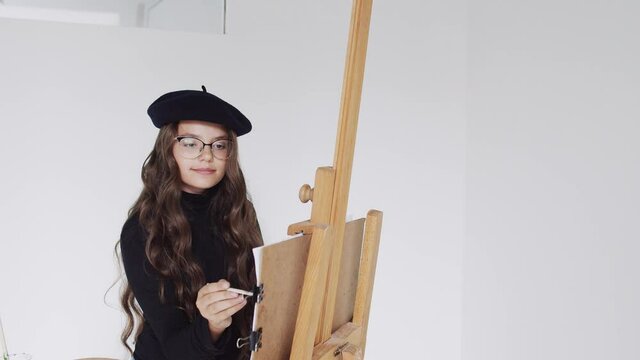 Young woman artist in beret painting picture on canvas in art studio