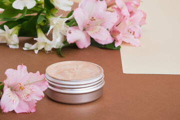 Obraz na płótnie Canvas aluminum cosmetic cream jar and beautiful pink and white lily flowers on beige brown background