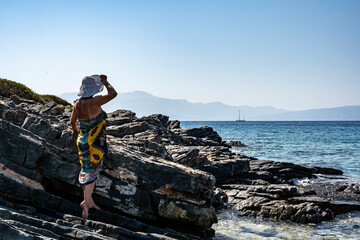 woman in white hat posing on stones against the background of the sea 