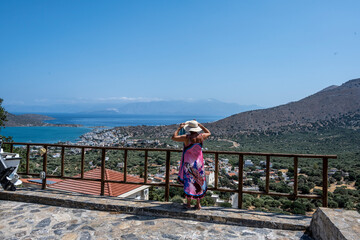 Fototapeta na wymiar woman in purple dress and white hat posing against the background of sea mountains and ancient ruins of the island of Crete 