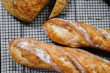 Fresh baked bread and baguettes on a cooling rack in a bakery.