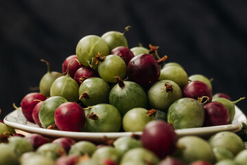 Gooseberry. Green and red gooseberry berries on a black background. Gooseberries on a white plate on a black background