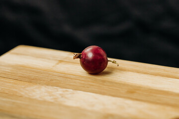 Gooseberry. One red berry. One gooseberry berry on a wooden surface. Plenty of space for text