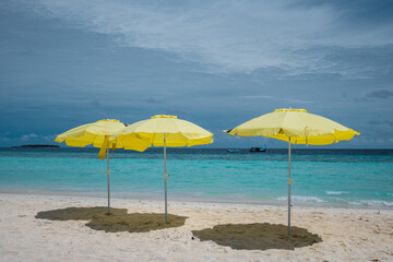 Yellow umbrellas on the white sand beach of the Maldives. Travel and recreation.