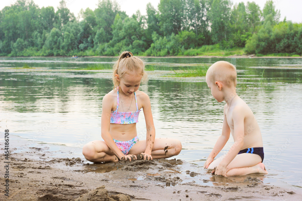 Wall mural girl and boy playing in the sand by the river, brother and sister are resting in nature