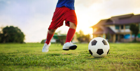 Boy kicking a ball while playing street soccer football on the green grass field for exercise. Outdoor sport activity for children and kids concept photo with copy space.