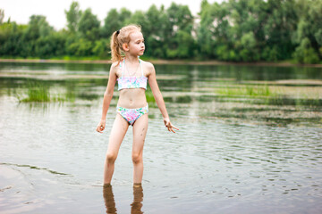 a little girl in a swimsuit stands in the river and looks into the distance, summer vacation with...