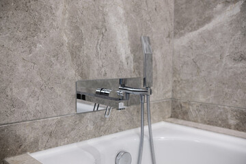 Details of bathroom, white bath tub with chrome faucet and a grey marble wall.