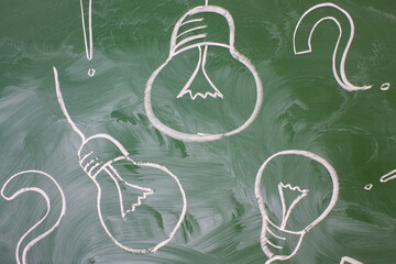 Electric lamps and question marks drawn in white chalk on a green blackboard and a space for copying. Concept ideas for study and business