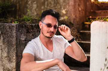 Attractive young man with transition lenses posing on a stairs outdoor. Waist up portrait of cool looking guy.