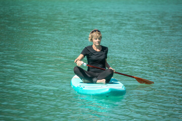 Obraz premium SUP concept surfboard - cute young woman is paddling on a beautiful lake with turquoise water