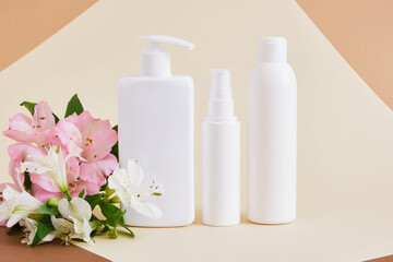 Fototapeta na wymiar lily flowers and three different white blank bottles of cosmetics on beige background