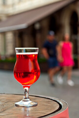 Glass of red wine close up. Alcoholic liqueur on a wooden barrel on a background of the city. Blurred people in the background.