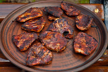 Grilled stew. Pieces of chop on a clay plate close up. Steaks on a brown plate.