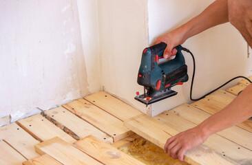 A man cuts a board with an electric saw. Repair of the floor in the house. Selective focus.