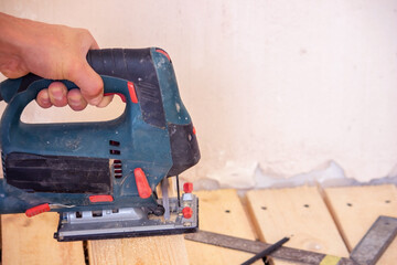 A man cuts a board with an electric saw. Repair of the floor in the house. Selective focus.