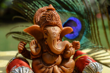 Fototapeta na wymiar Beautiful lord Ganesha idol worshipped during Ganesh chaturthi festival with peacock feather in background. Sitting Ganpati with pillows and bolsters during Vinayaka chavithi