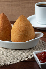 Delicious snack coxinha of chicken in white bowl and black coffee.