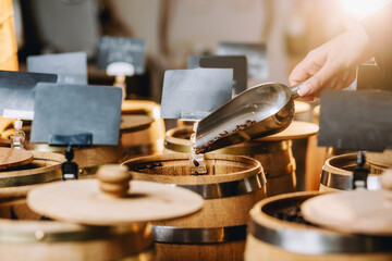 Closeup of female hand holding metal scoop full of coffee beans in coffee shop