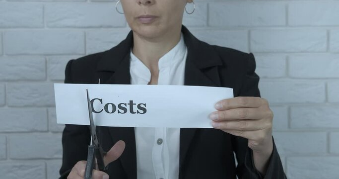 Businesswoman cut costs. A businesswoman cut paper with word costs in the office.