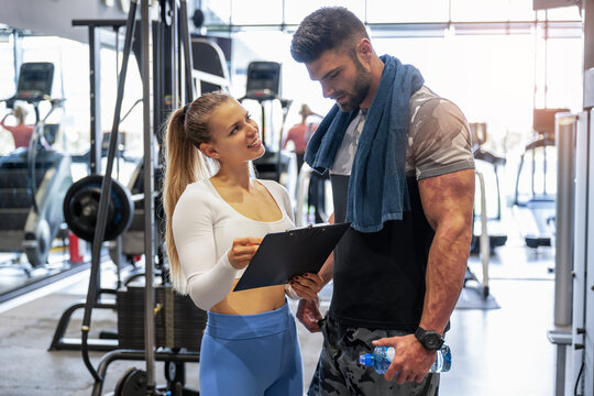 Female personal trainer showing exercise progress to her male client in a gym.