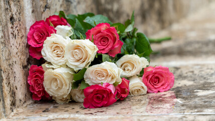 Close-up on a bouquet of roses, white and pink, on a paved outdoor floor, in rainy weather