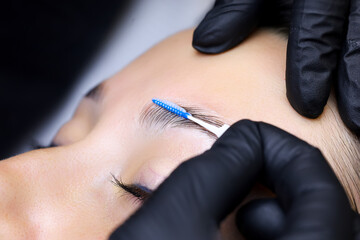 close-up of the master's hands holding a micro brush that combs the eyebrows and models after the eyebrow lamination procedure - obrazy, fototapety, plakaty