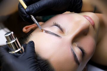 close-up of the master combs the eyebrows of the model with a brush after the procedure of...