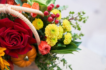 Close-up of a basket with beautiful autumn flowers made of red roses, sunflowers and green leaves. The concept of the holiday. Copy space. High quality photo