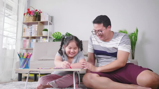 Happy Asian father playing with daughter having fun spending free leisure time painting on paper. Having a funny conversation. Painting with color pencil in living room at home. Happy fat family