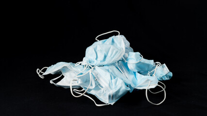 Pile of used surgical masks, blue and white, piled on top of each other, on black background