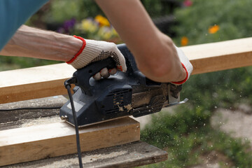 A carpenter planks wood with an electric plane. Woodworking carpentry. Close-up. Man in the garden...