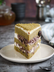 Traditional Japanese green matcha red bean paste cream mascarpone filling chiffon sponge cake in a white plate with tea pot and cup in background.  A light soft texture with a hint of matcha flavour