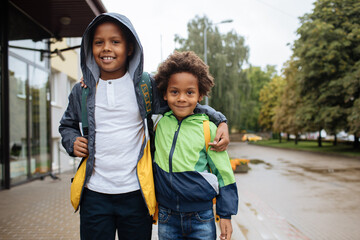 Little boys with back packs. Two African American boys next to the school. Back to the school concept. Kids standing outside and happy to meet each others. Happy black children. First day of school